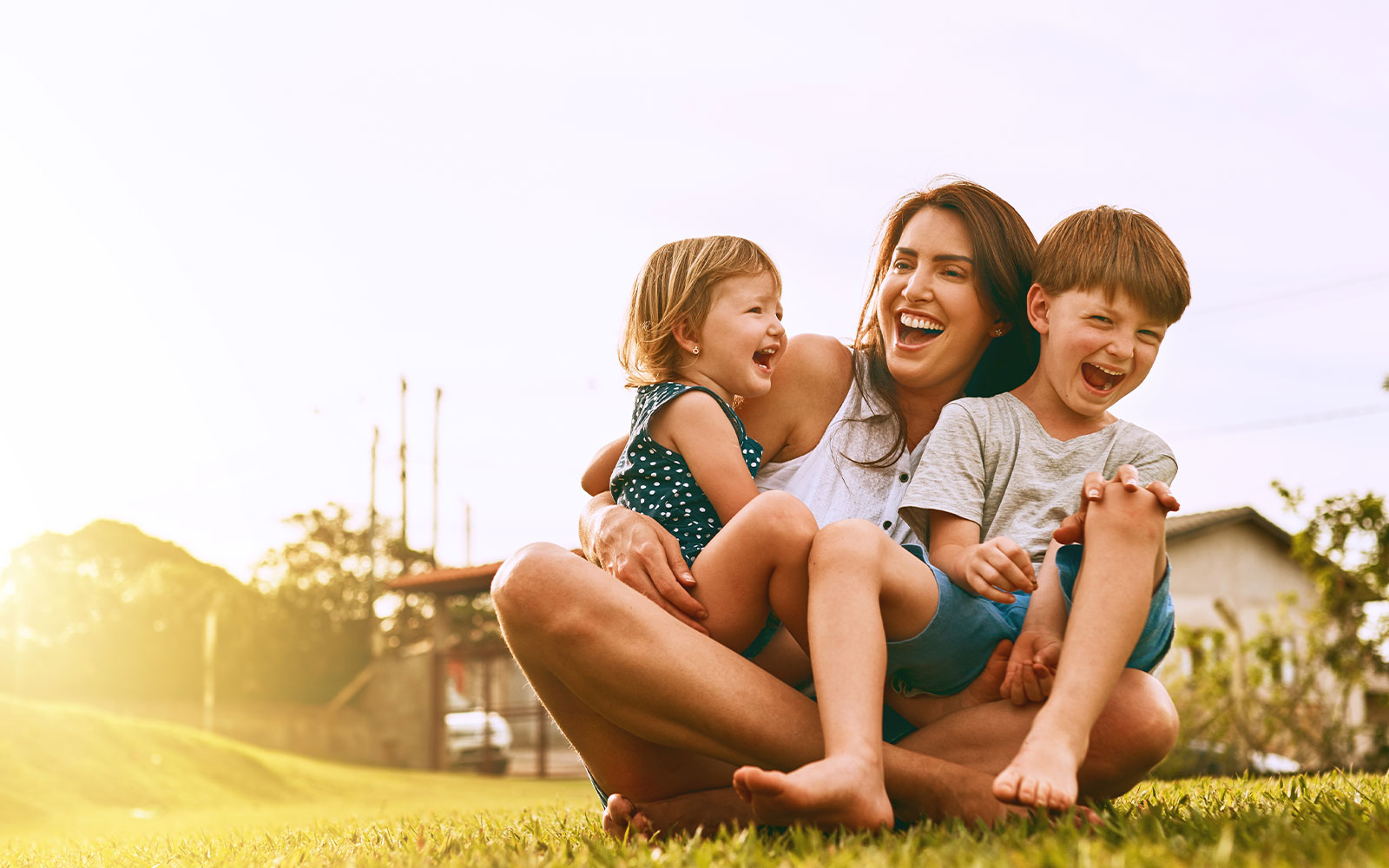 A family of three, with a woman and two children, sitting on the grass outdoors during sunset.