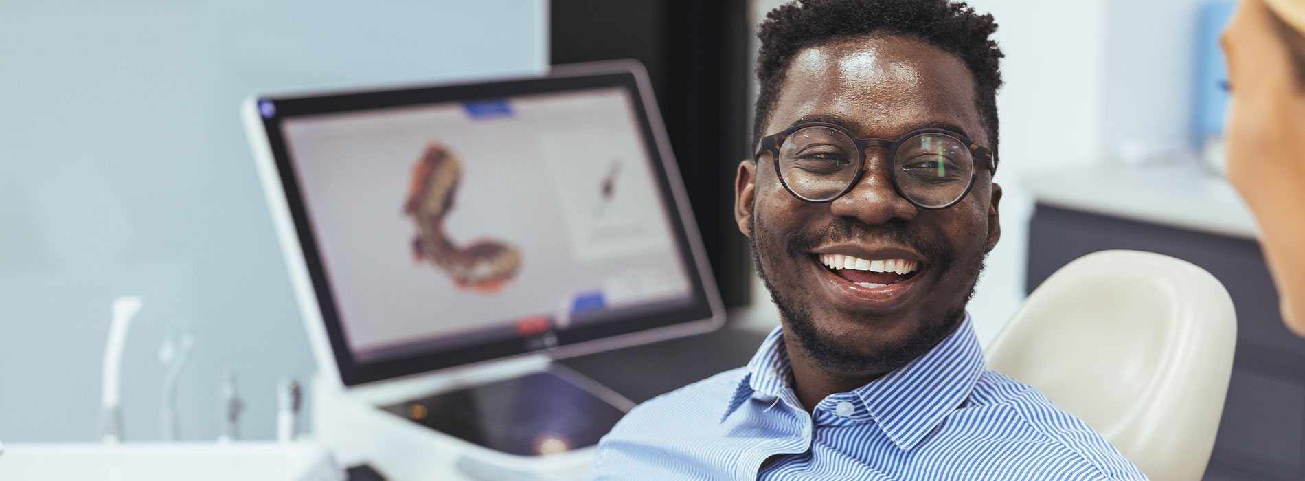 A man is seated in front of a computer screen, smiling broadly as if he s in a good mood or sharing something amusing.