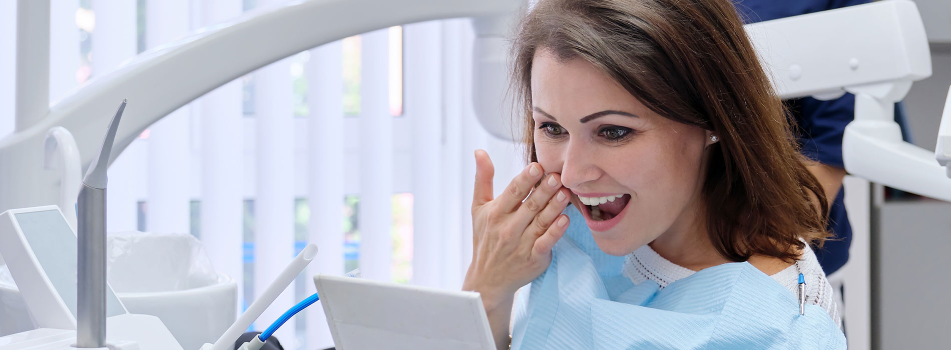 A woman in a dental office, sitting at a desk with her mouth open, holding what appears to be a toothbrush or dental tool.