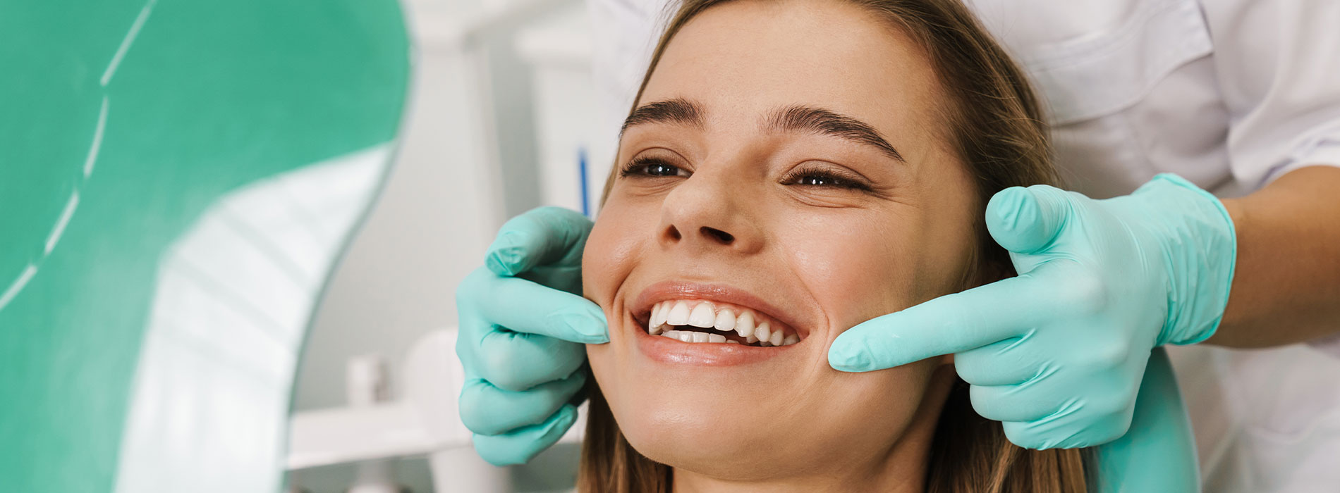 A woman receiving dental care, seated in a dental chair with a smiling expression, while a dental professional adjusts her teeth.