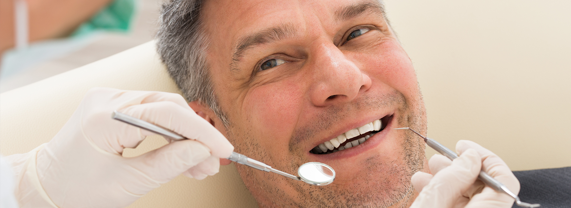 A man is sitting in a dental chair, receiving dental care with a smile on his face.