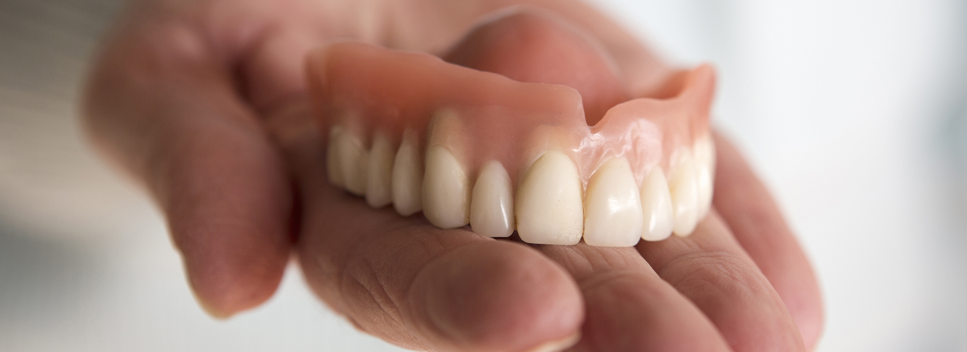 The image shows a person holding up a set of dentures, with the focus on the lower front teeth.