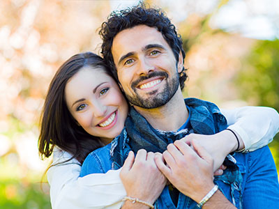 A man and a woman embracing, smiling, with the man wearing a scarf around his neck.