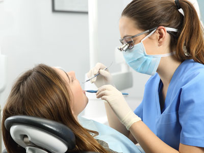 A dental hygienist in a white coat and blue gloves is attending to a patient s teeth while the patient sits comfortably in the chair.