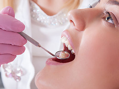 Dental care professional performing oral examination on patient, with focus on teeth cleaning tool.