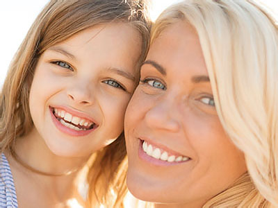 A smiling woman and a child, both with blue eyes, enjoying a sunny day together.