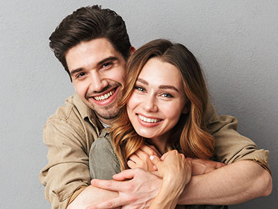 A man and a woman are embracing each other in a warm pose, both smiling at the camera.