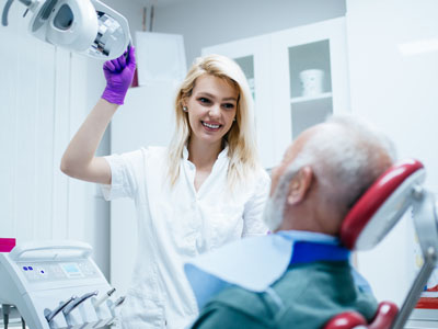 A dental professional is assisting an elderly patient with a dental procedure, using a dental chair and equipment.