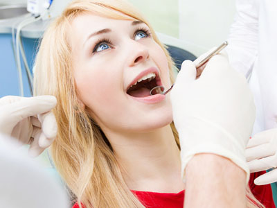 A young woman in a dental chair, smiling and receiving dental care from a professional, with medical equipment visible.